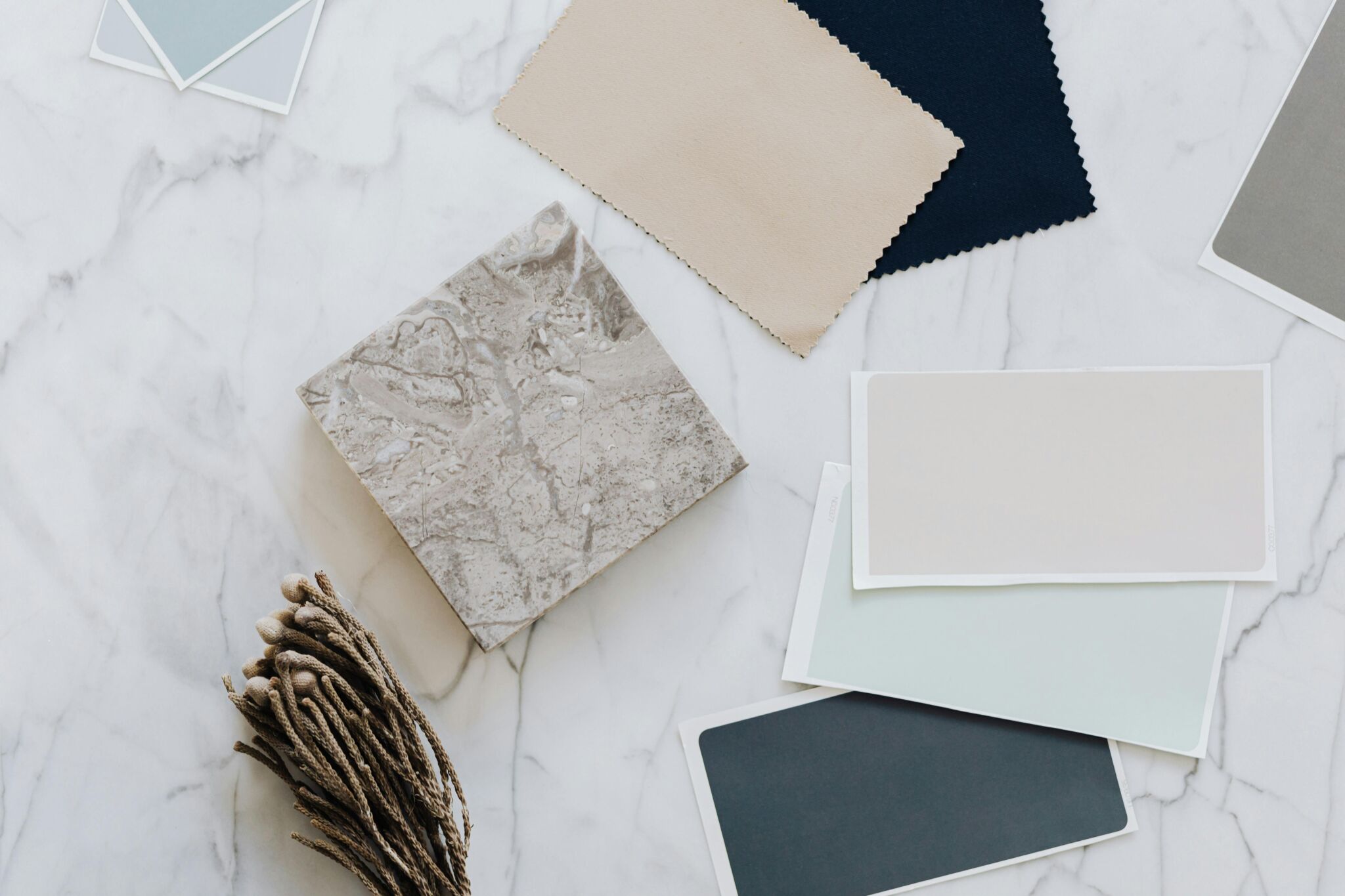 An artistic flat lay showcasing diverse fabric and material samples on a marble surface, emphasizing neutral tones and textures.